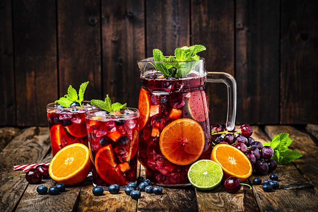 Jarro e copos com sangria sem álcool, decorados com frutas cítricas, uvas e folhas de hortelã, sobre uma mesa de madeira rústica