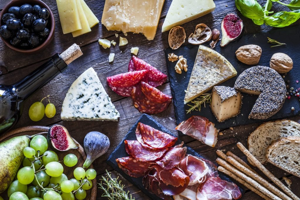 Mesa de frio com queijos, embutidos, frutas frescas e secas, acompanhada de pão e vinho