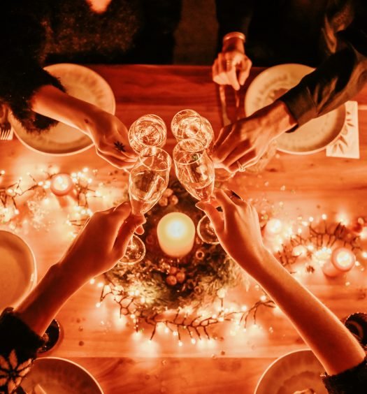 Pessoas brindando com taças de prosecco em uma mesa decorada com luzes e velas