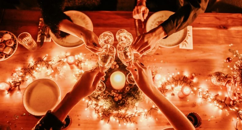 Pessoas brindando com taças de prosecco em uma mesa decorada com luzes e velas