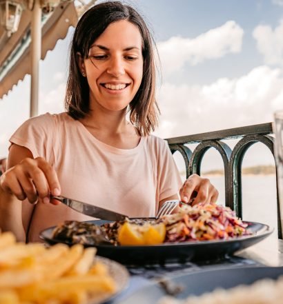 Mulher sorrindo enquanto come uma refeição em um restaurante à beira-mar