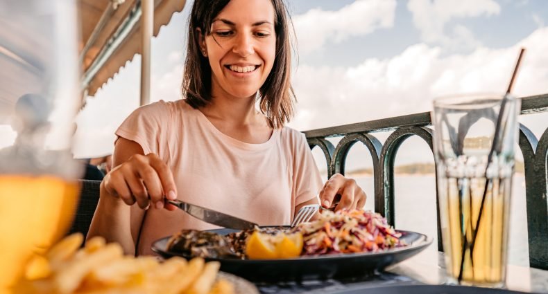 Mulher sorrindo enquanto come uma refeição em um restaurante à beira-mar