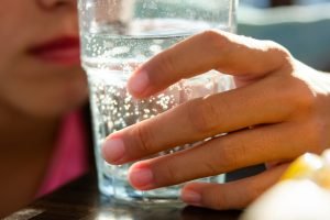 Mão segurando um copo de água com gás.