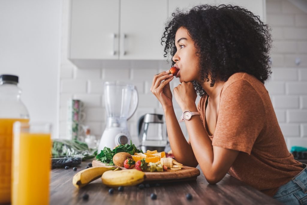 Mulher comendo frutas e legumes em uma mesa