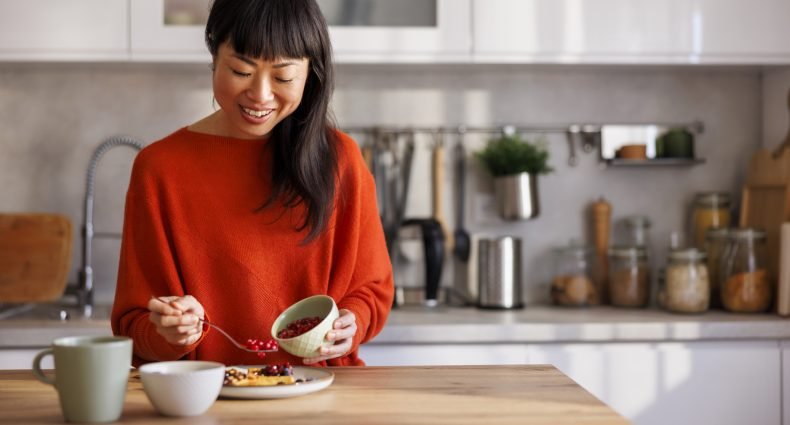 Mulher sorrindo enquanto prepara uma refeição