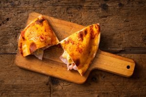 Calzone recheado de presunto e queijo em uma tábua de madeira