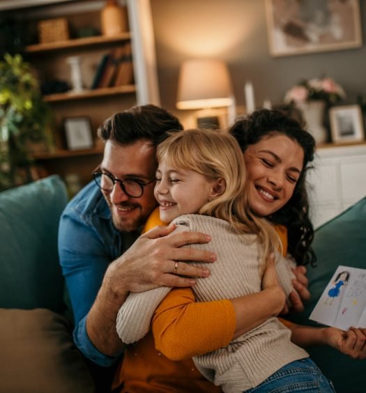 Família feliz se abraçando no sofá verde