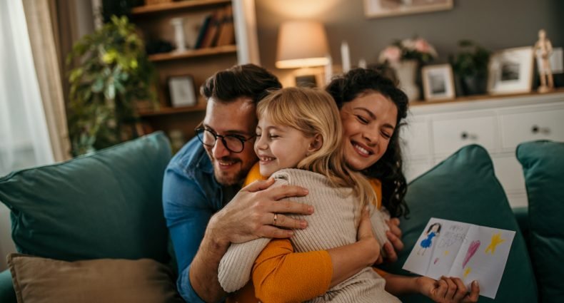 Família feliz se abraçando no sofá verde