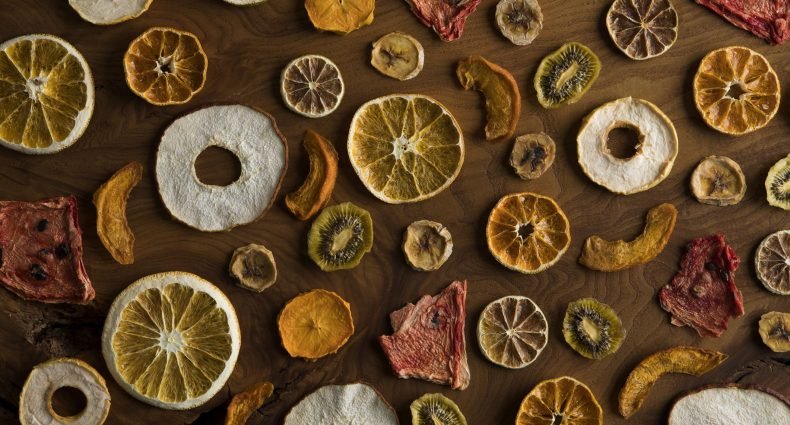 Fatias de frutas desidratadas organizadas sobre uma mesa de madeira.
