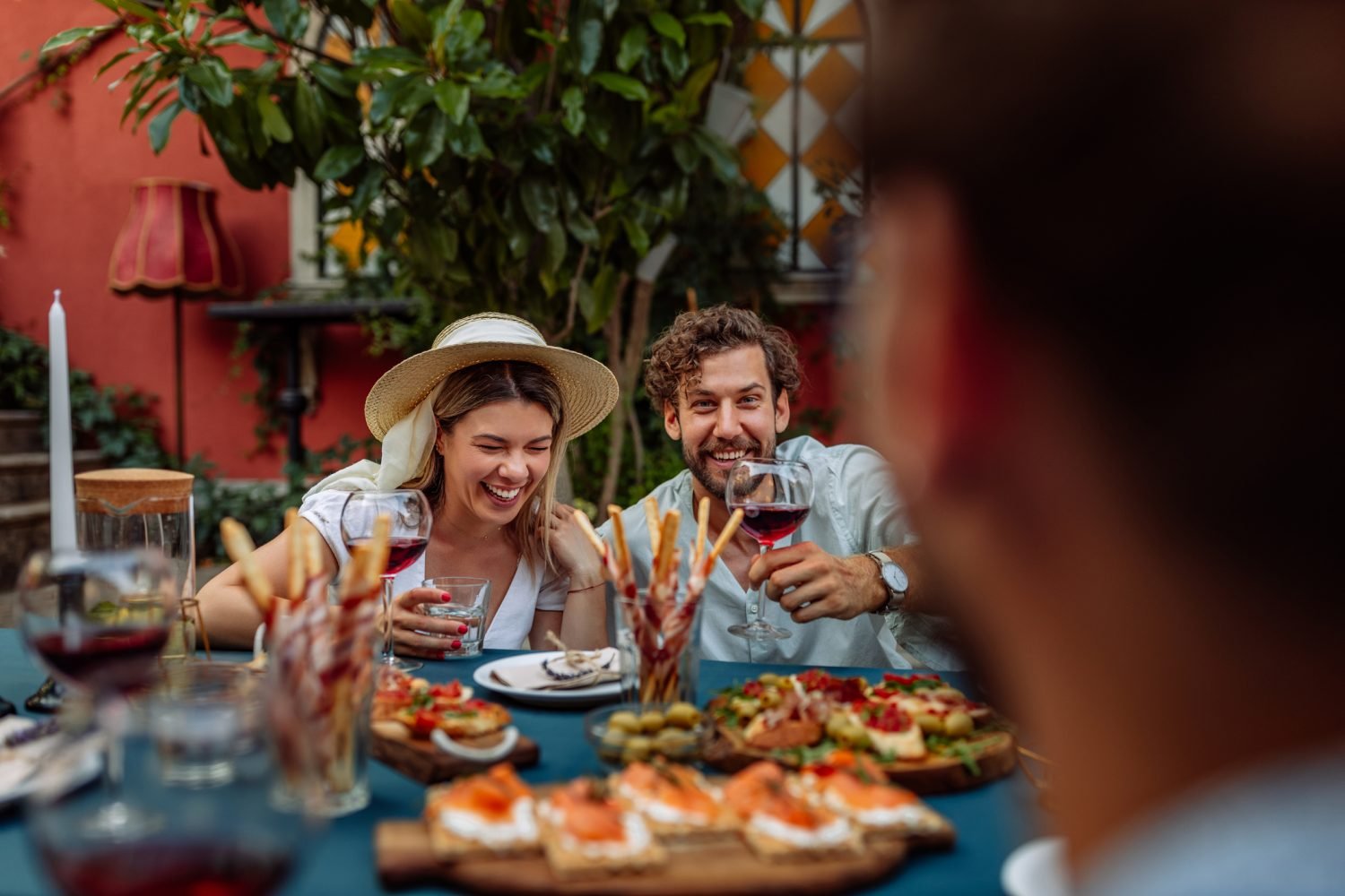 Casal se divertindo em um jantar ao redor de uma mesa cheia de pratos e vinhos.