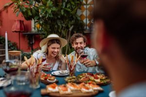 Casal se divertindo em um jantar ao redor de uma mesa cheia de pratos e vinhos.