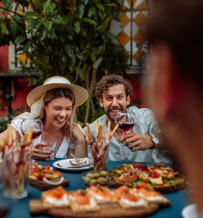 Casal se divertindo em um jantar ao redor de uma mesa cheia de pratos e vinhos.