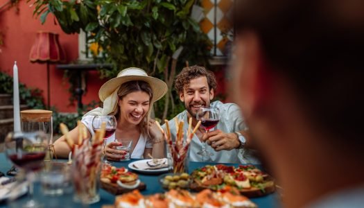 Casal se divertindo em um jantar ao redor de uma mesa cheia de pratos e vinhos.