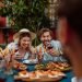 Casal se divertindo em um jantar ao redor de uma mesa cheia de pratos e vinhos.