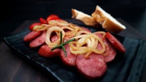 Linguiças grelhadas com cebolas em prato.