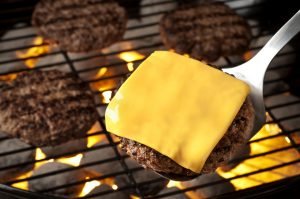 Queijo cheddar sendo adicionado a hambúrguer na churrasqueira