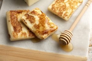 Queijo coalho grelhado com mel sobre tábua.