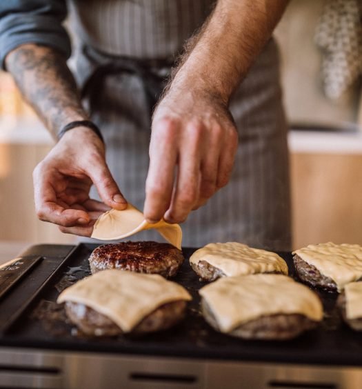Queijo derretendo sobre hambúrguer na grelha