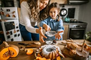 Mãe e filha polvilhando açúcar em um bolo bundt criando receitas de outono