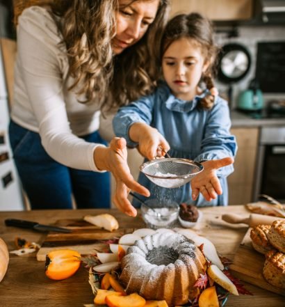 Mãe e filha polvilhando açúcar em um bolo bundt criando receitas de outono