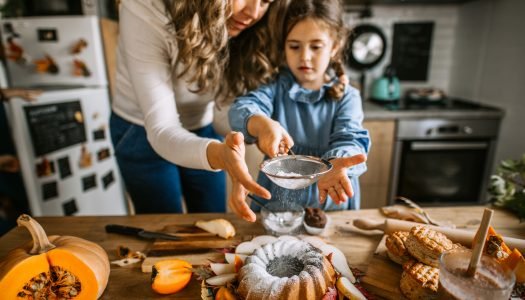 Mãe e filha polvilhando açúcar em um bolo bundt criando receitas de outono