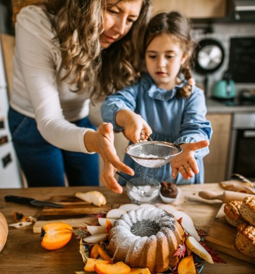 Mãe e filha polvilhando açúcar em um bolo bundt criando receitas de outono