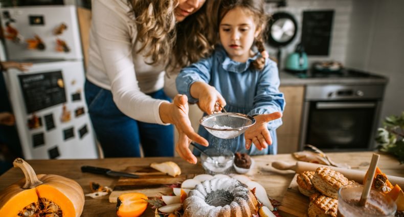 Mãe e filha polvilhando açúcar em um bolo bundt criando receitas de outono