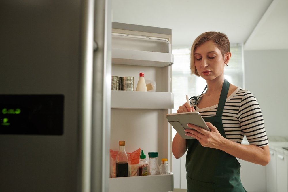 Mulher fazendo lista de compras na cozinha