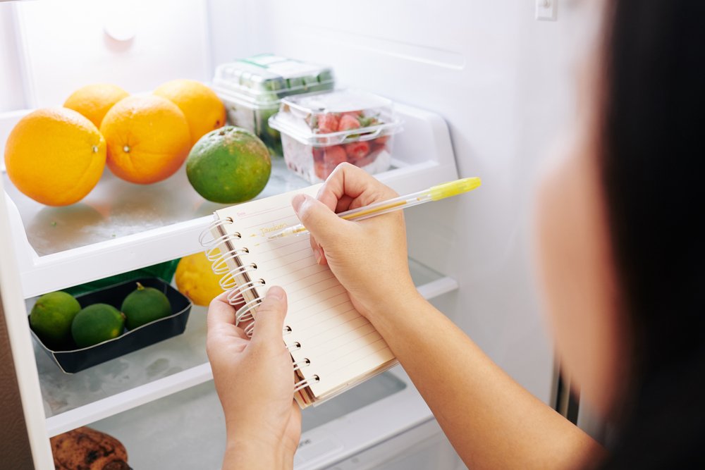 Mãos fazendo anotações de compras na geladeira