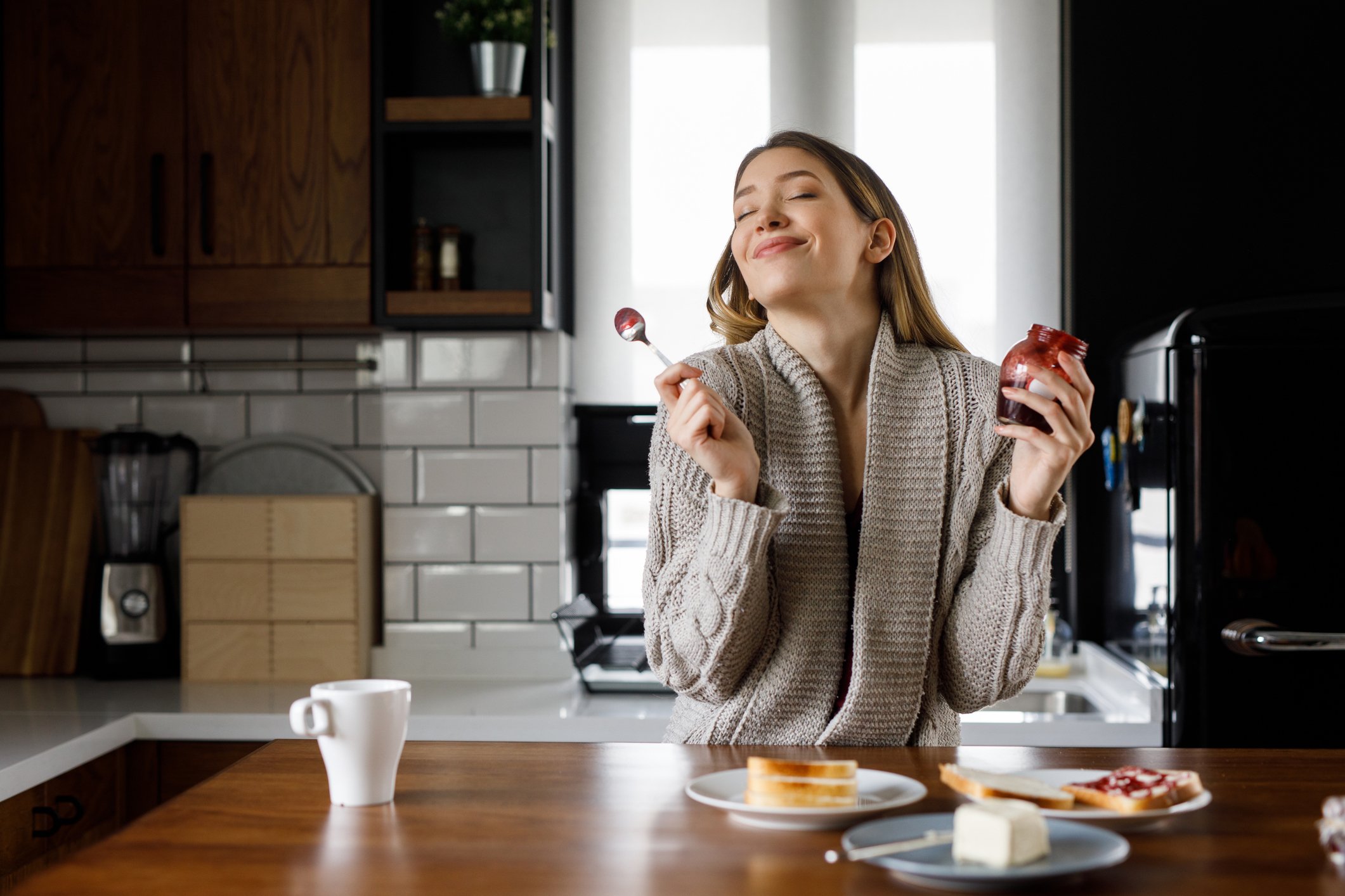 Mulher feliz saboreando sobremesas com uma xícara de café ao lado.