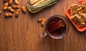 Quentão com cachaça, canela e amendoim ao lado de milho.