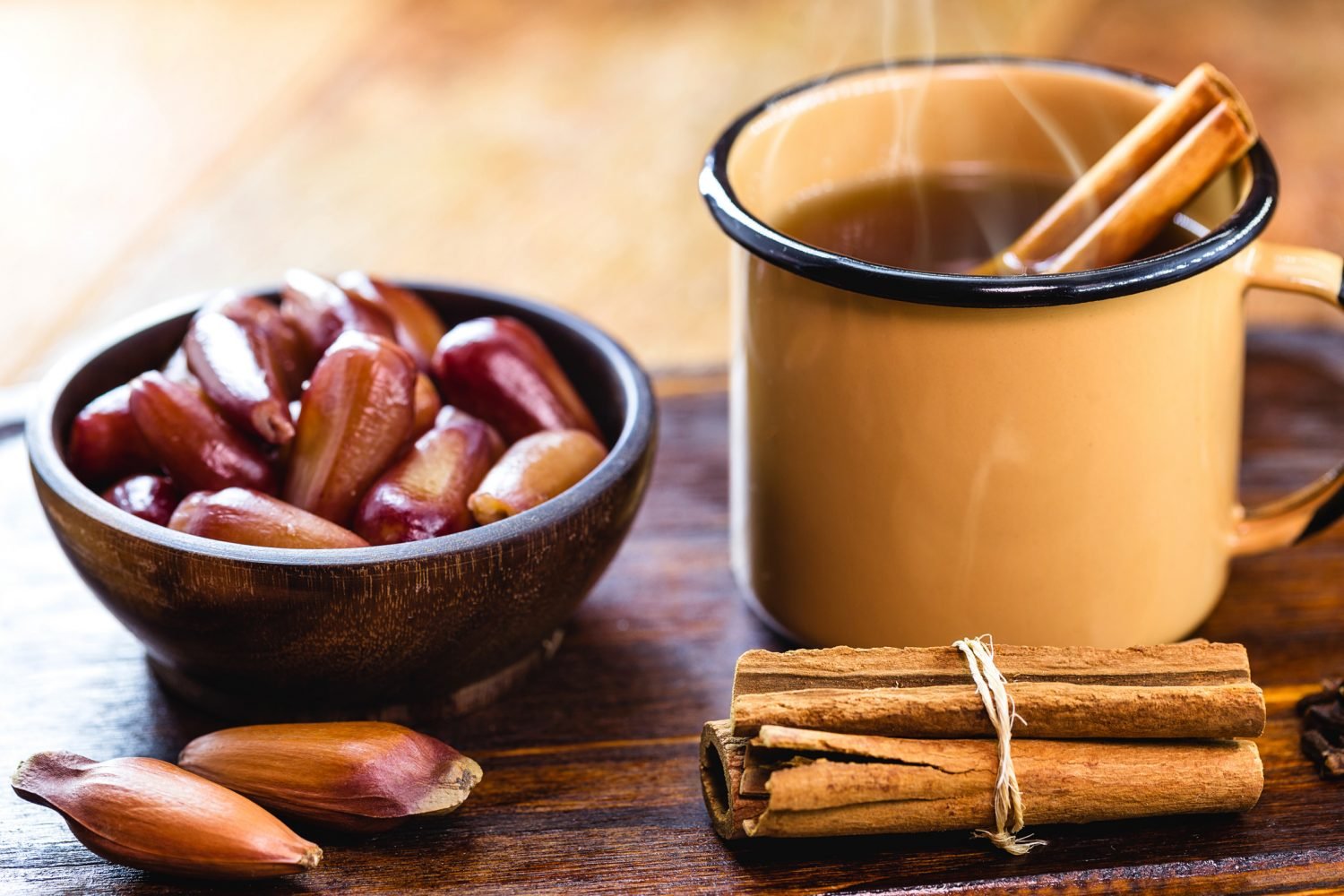 Xícara de quentão com canela ao lado de uma tigela com pinhão.