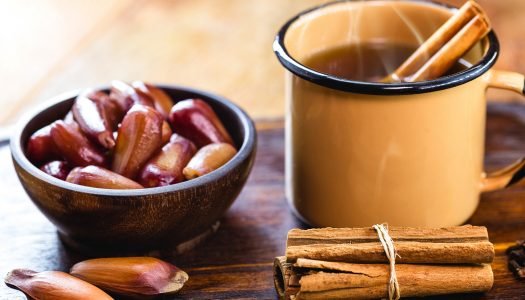 Xícara de quentão com canela ao lado de uma tigela com pinhão.