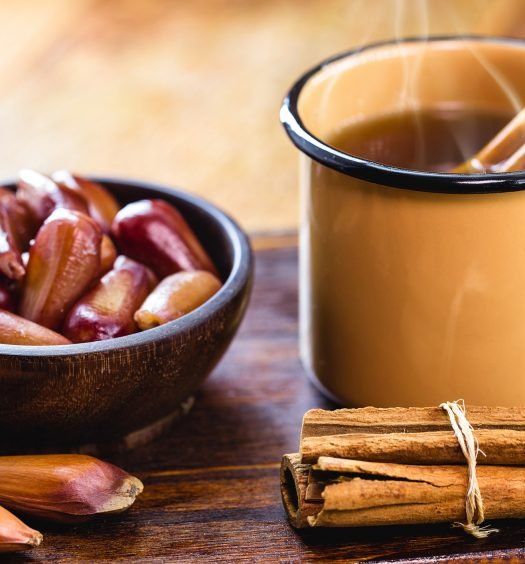 Xícara de quentão com canela ao lado de uma tigela com pinhão.