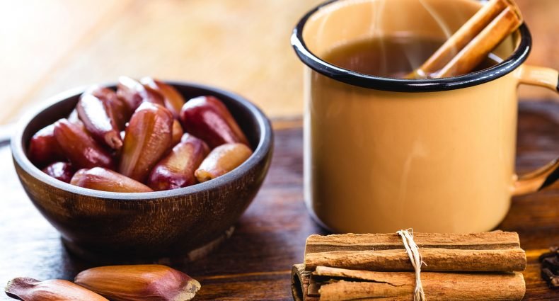 Xícara de quentão com canela ao lado de uma tigela com pinhão.