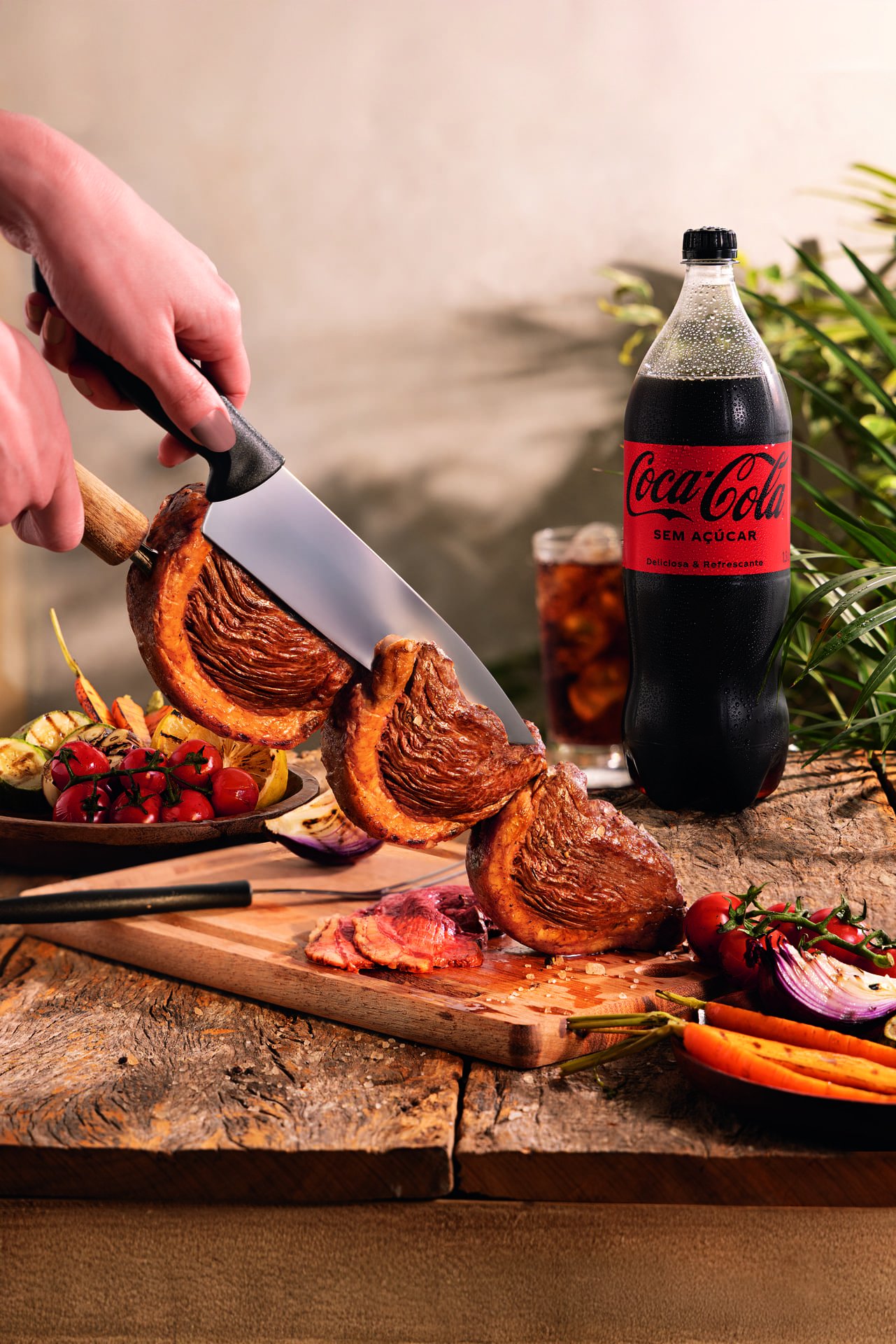 Homem cortando carne suculenta com uma faca, ao lado de uma garrafa de Coca-Cola e acompanhamentos em um ambiente de churrasco para o Dia dos Pais.