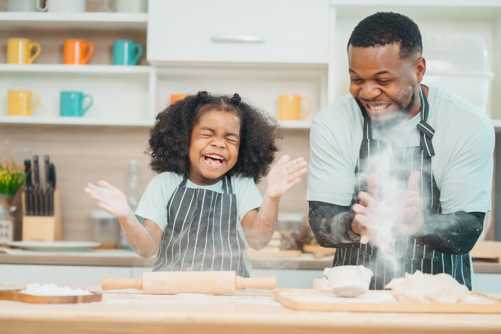 Pai e filha se divertindo enquanto cozinham juntos.
