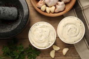 Dois recipientes de molho de alho cremoso ao lado de alho.