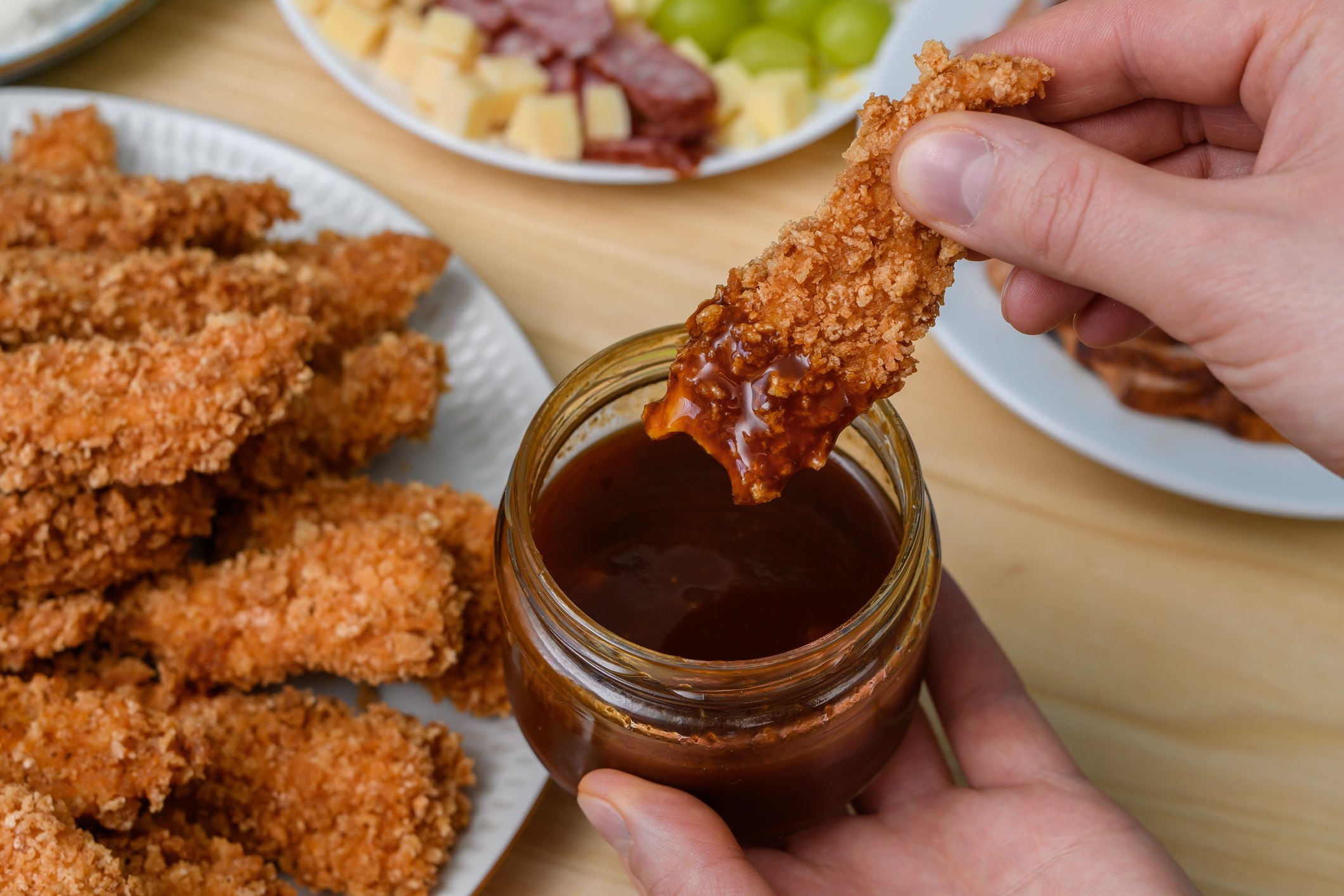 Mão mergulhando frango empanado em molho barbecue.
