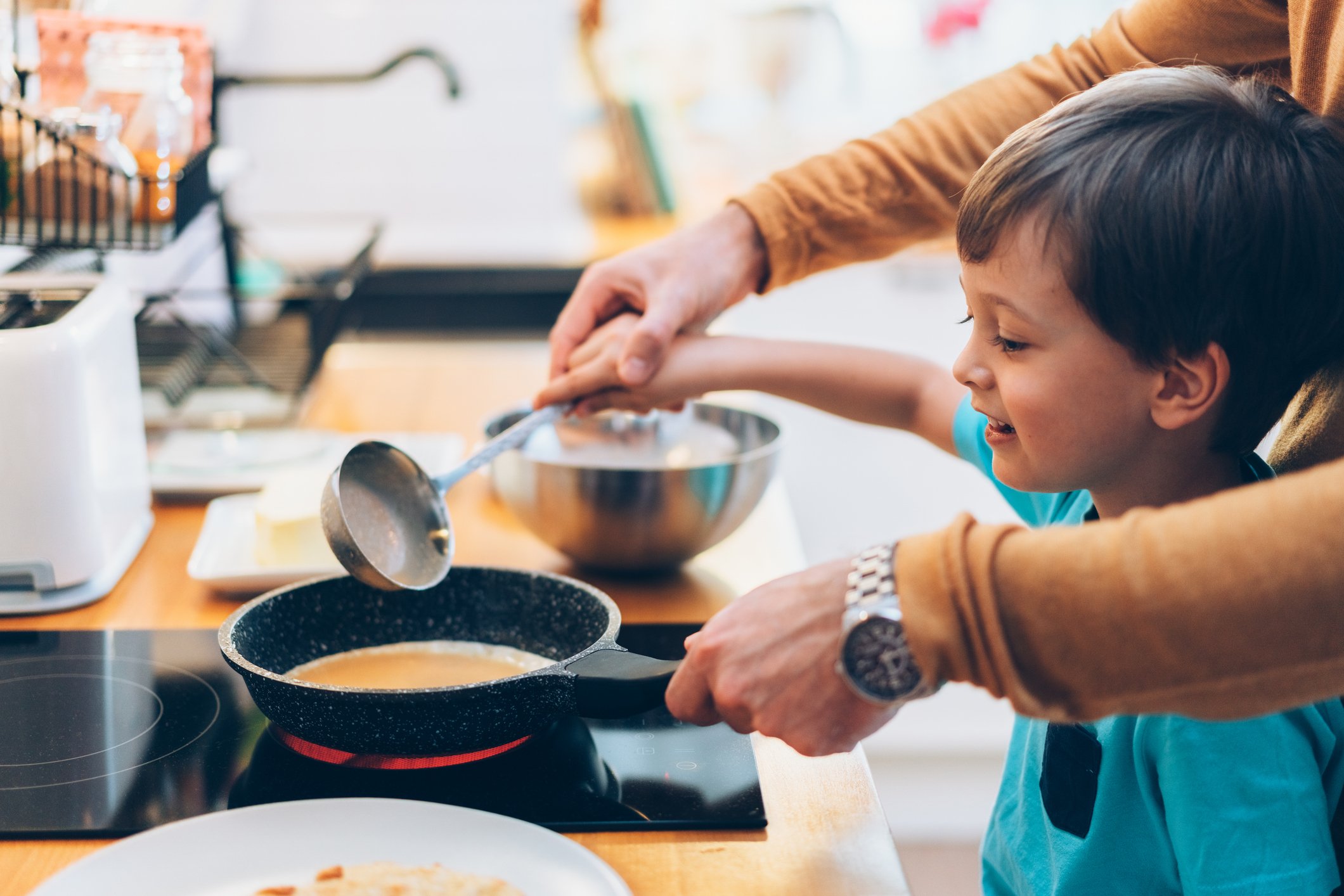 Criança aprendendo a fazer panquecas com pai na cozinha