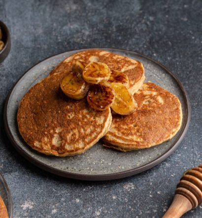 Panquecas de banana fit servidas em prato com fatias de banana e mel.