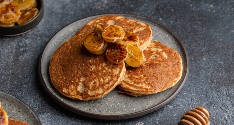 Panquecas de banana fit servidas em prato com fatias de banana e mel.