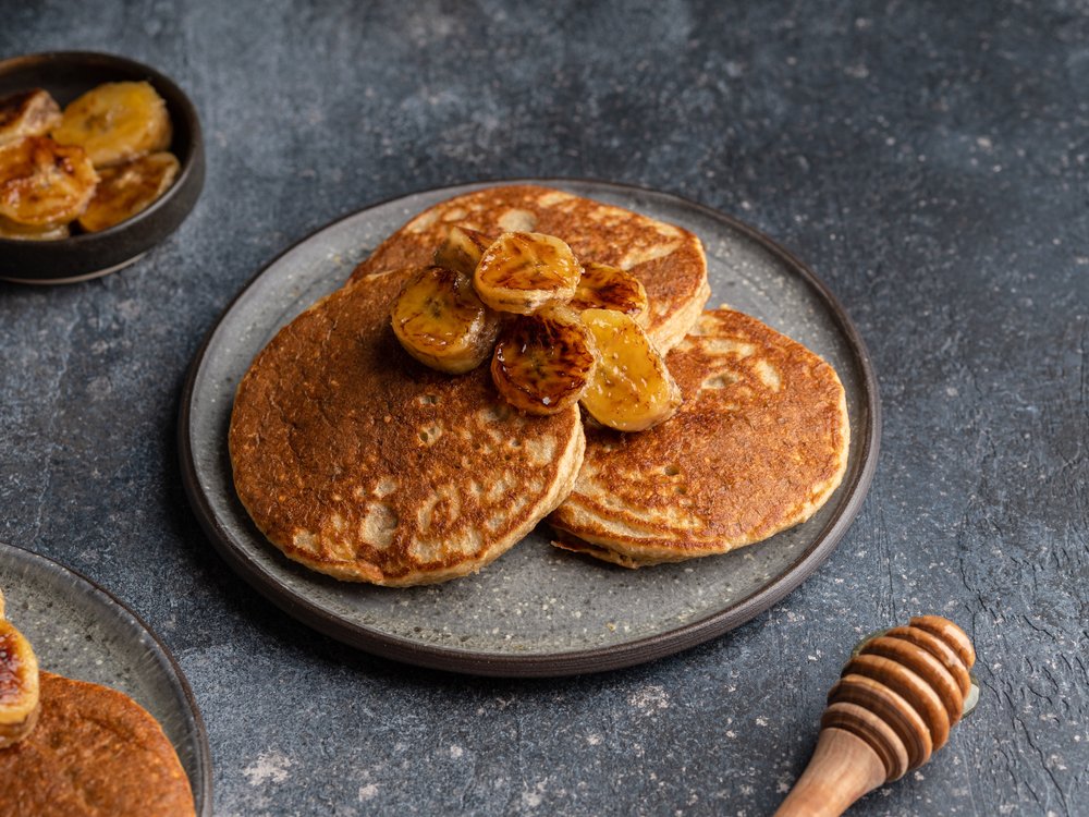 Panquecas de banana fit servidas em prato com fatias de banana e mel.