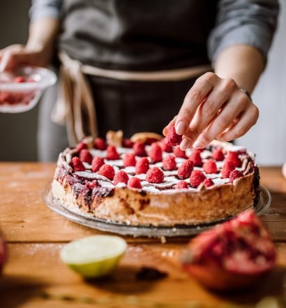 Mulher adicionando frutas em torta de morangos frescos.