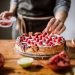Mulher adicionando frutas em torta de morangos frescos.