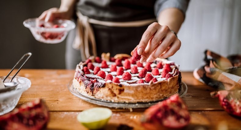 Mulher adicionando frutas em torta de morangos frescos.