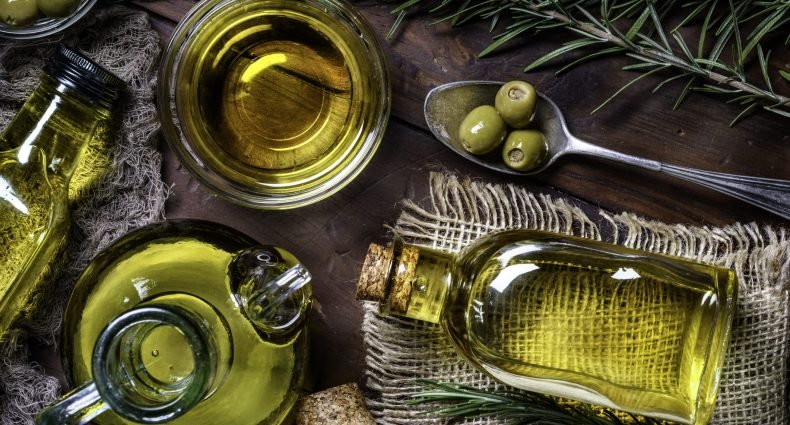 Azeite em diferentes recipientes ao lado de ramos de alecrim e azeitonas verdes