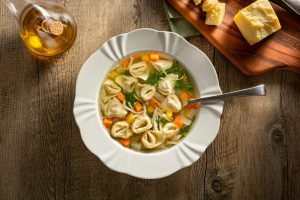 Sopa de capeletti com legumes coloridos em um prato raso