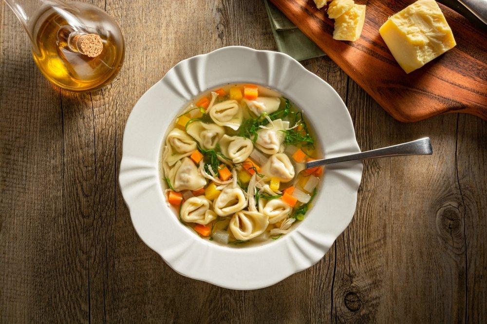Sopa de capeletti com legumes coloridos em um prato raso