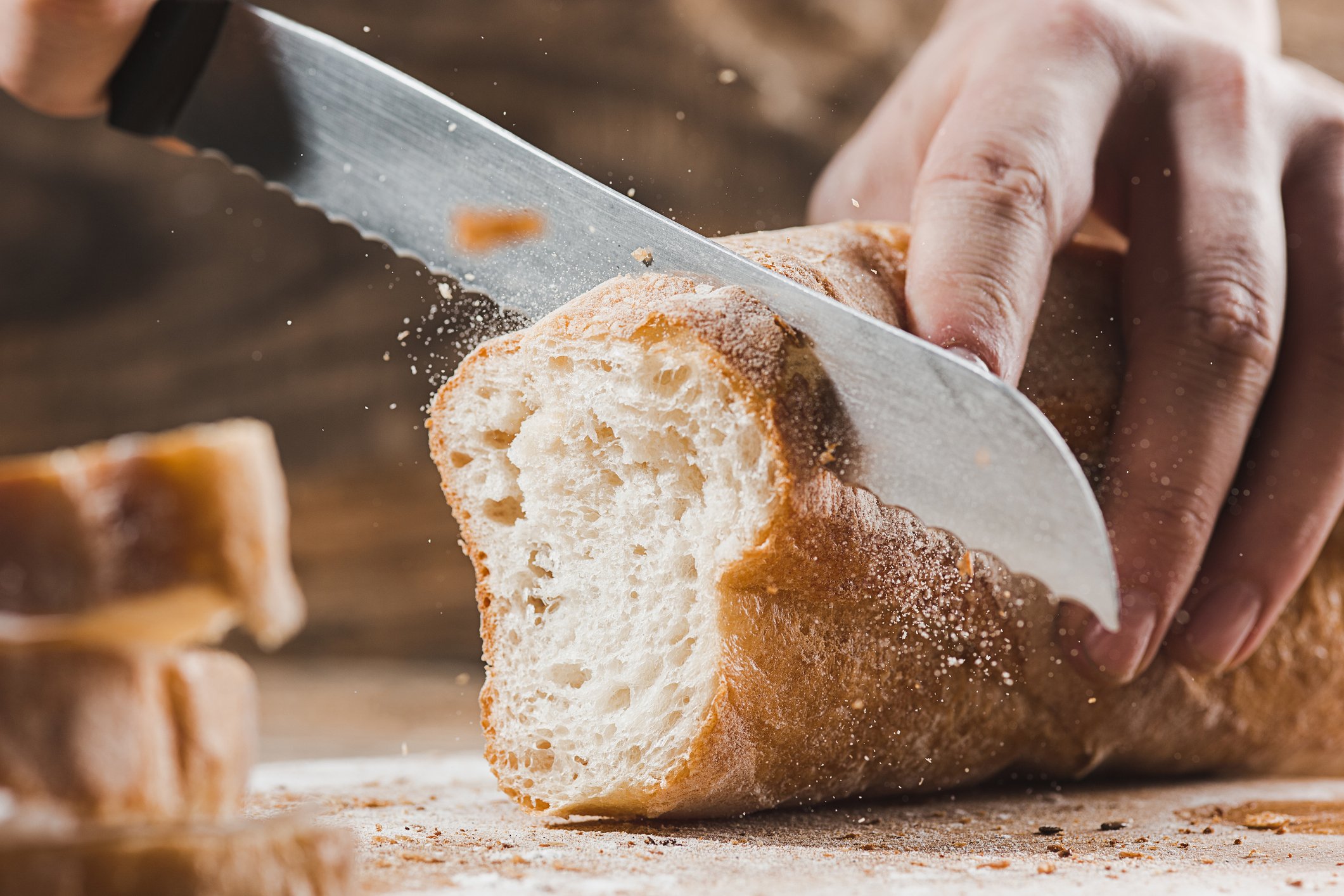 Mão cortando pão fresco.